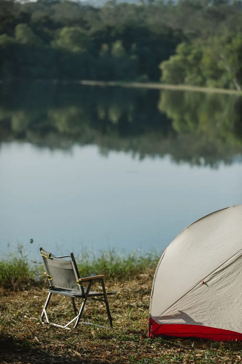 Folding chair beside a tent on a grassy lakeshore