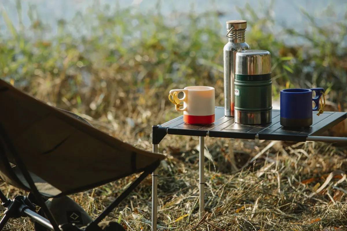 Thermos flasks and mugs on a lakeside camping table