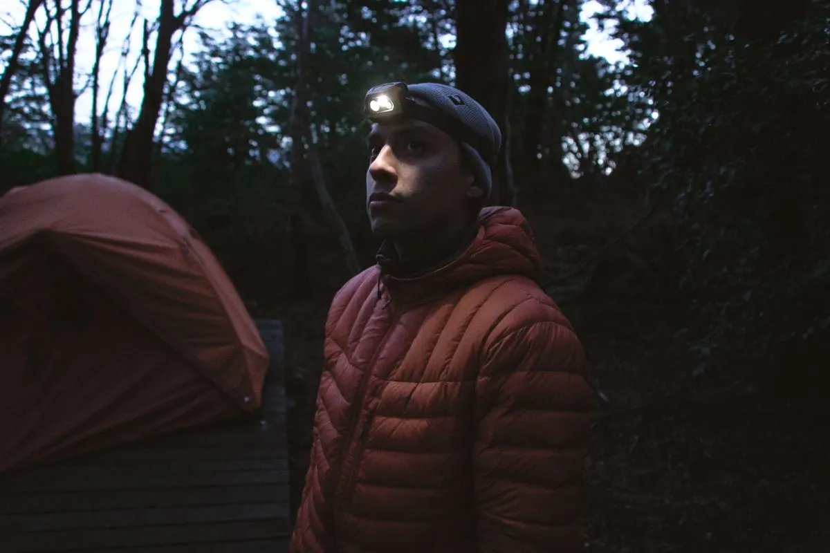 Camper wearing a headlamp beside a tent in a forest